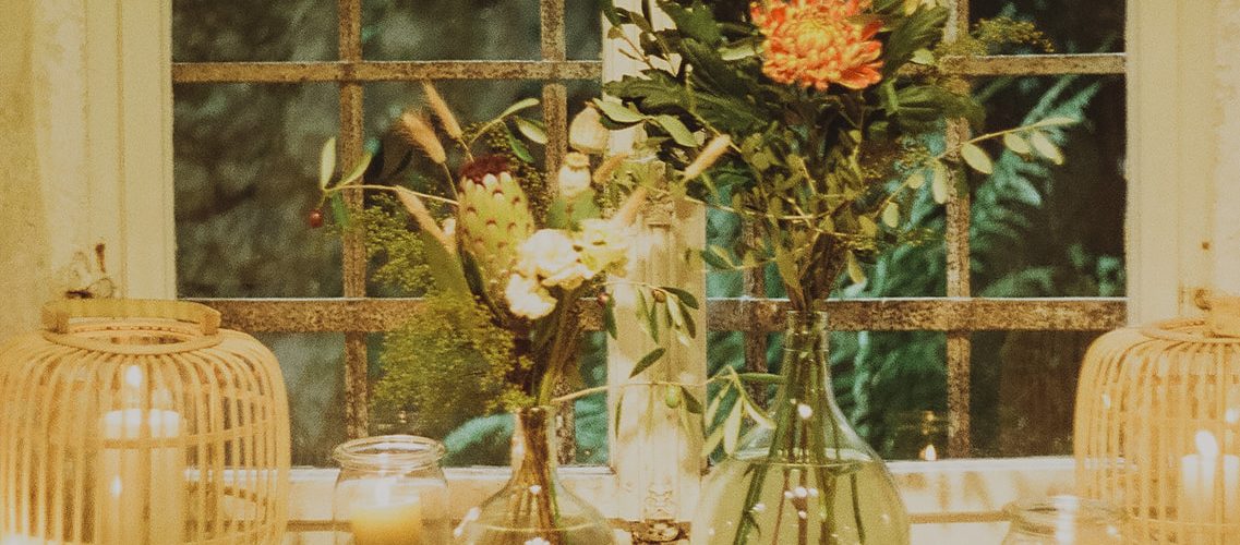Fenster mit grossem Sims in dicken Mauern von einem historischen Gebäude. Auf dem Sims stehen Blumen in Vasen und Kerzen in hübschen Gefässen.